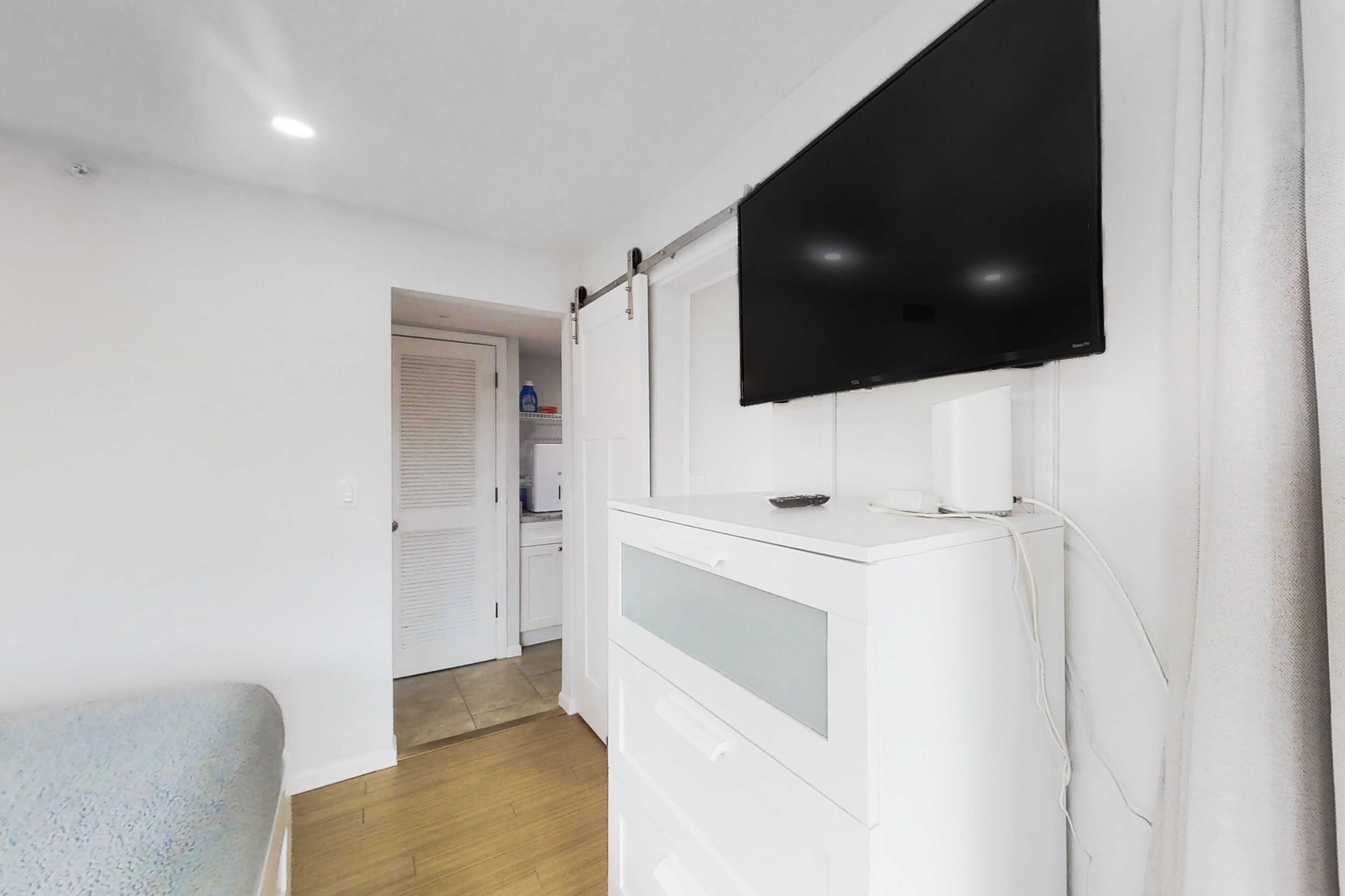 A room with a flat-screen TV mounted on the wall, a white cabinet with drawers, and a wooden floor.
