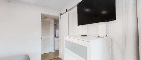 A room with a flat-screen TV mounted on the wall, a white cabinet with drawers, and a wooden floor.