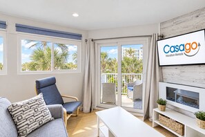 A modern living room with a sofa, armchair, and a flat-screen TV mounted on the wall. - Renovated Condo With Ocean Views, Pool, & Beach Access (Jacksonville Beach)