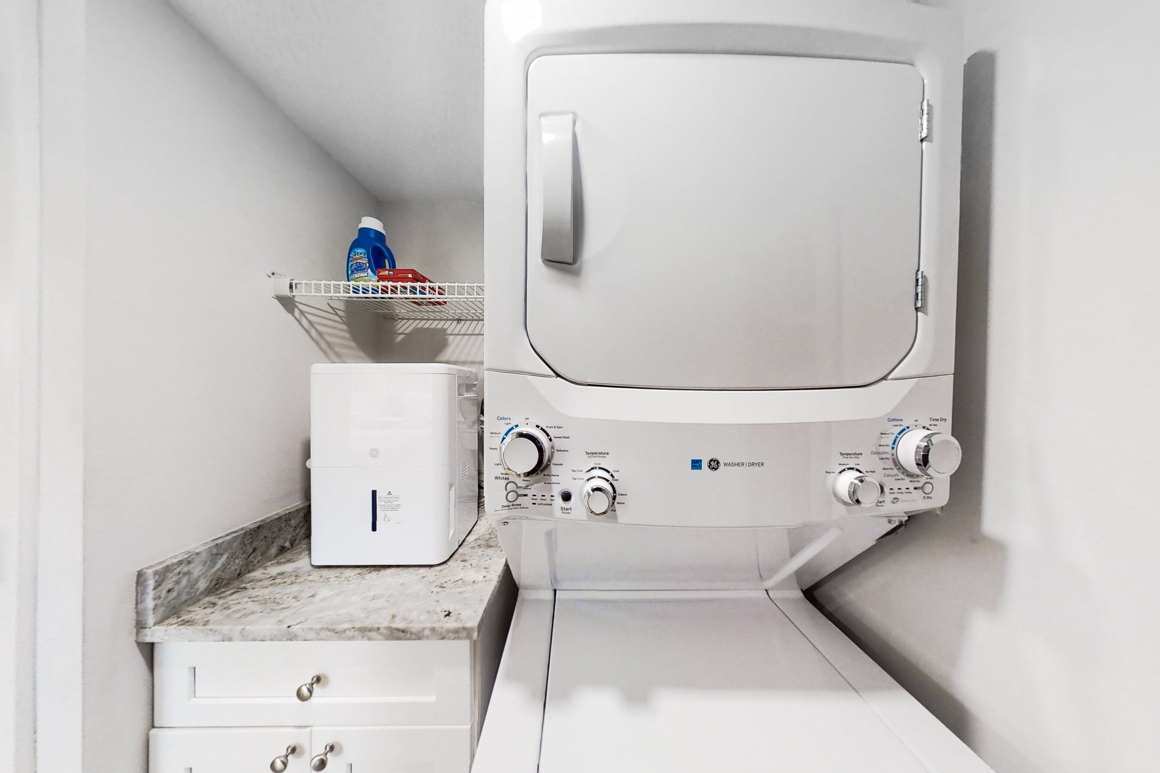 A compact laundry area with a washing machine and dryer, a small shelf with cleaning supplies, and a marble countertop.