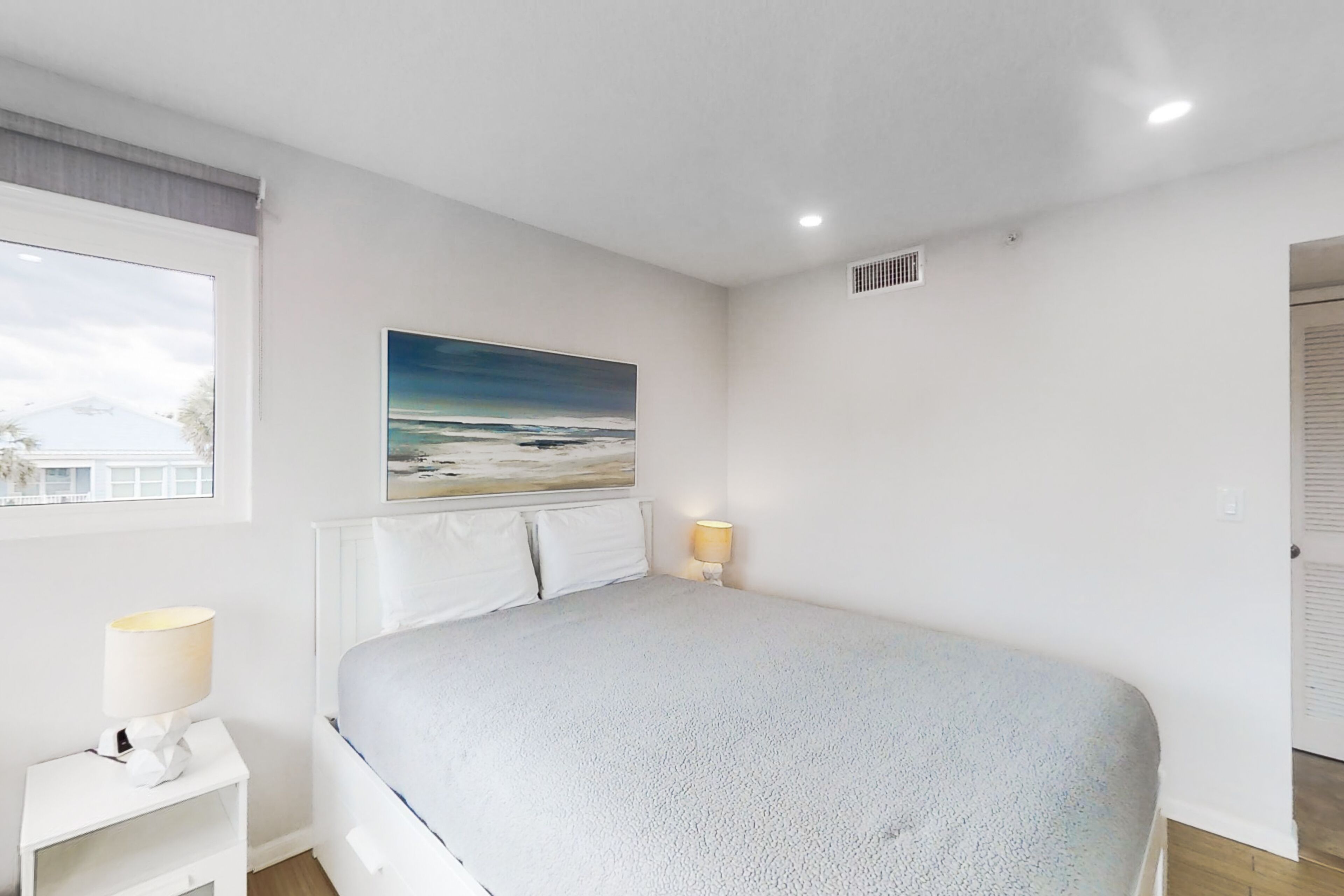 Une chambre à coucher avec un lit, une table de chevet, une lampe, un tableau et une fenêtre.
