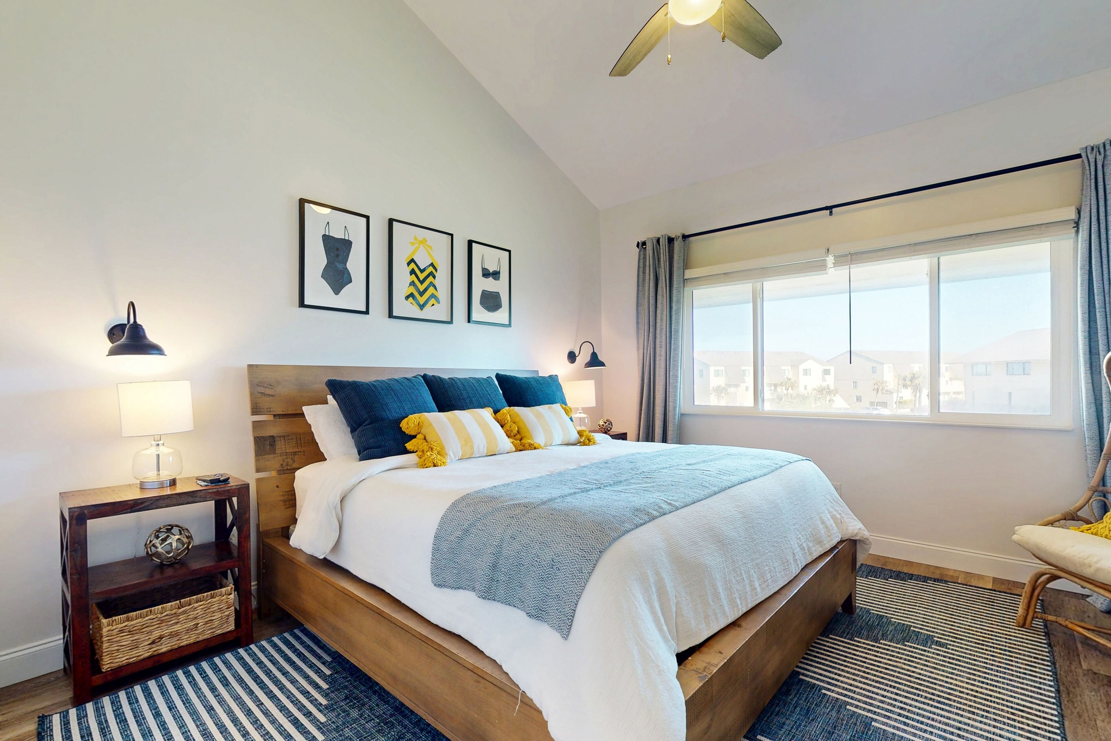 Un dormitorio con una cama grande, una mesita de noche de madera, una lámpara, una ventana con cortinas y vistas a la ciudad.