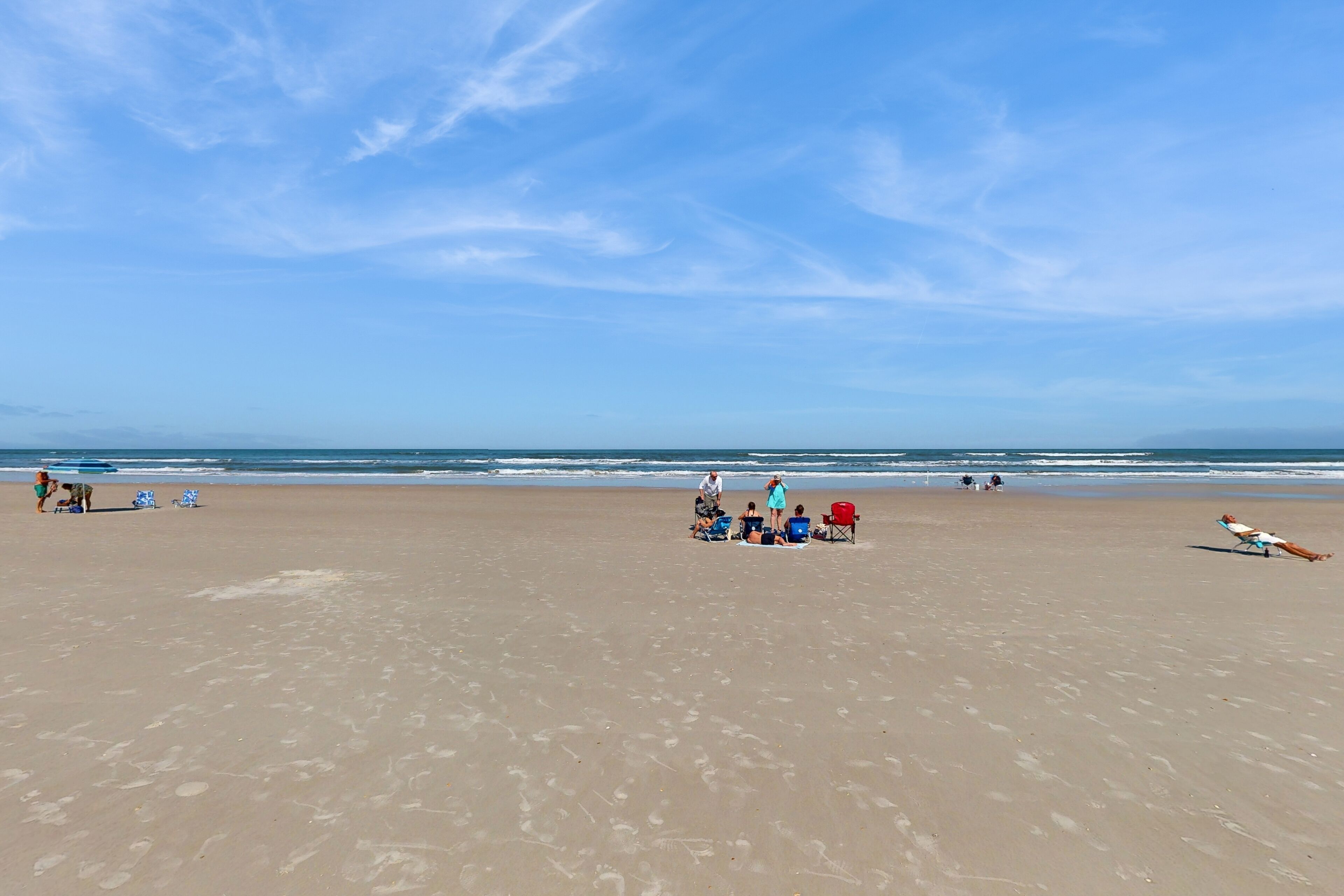Una amplia playa de arena con huellas y algunas personas.