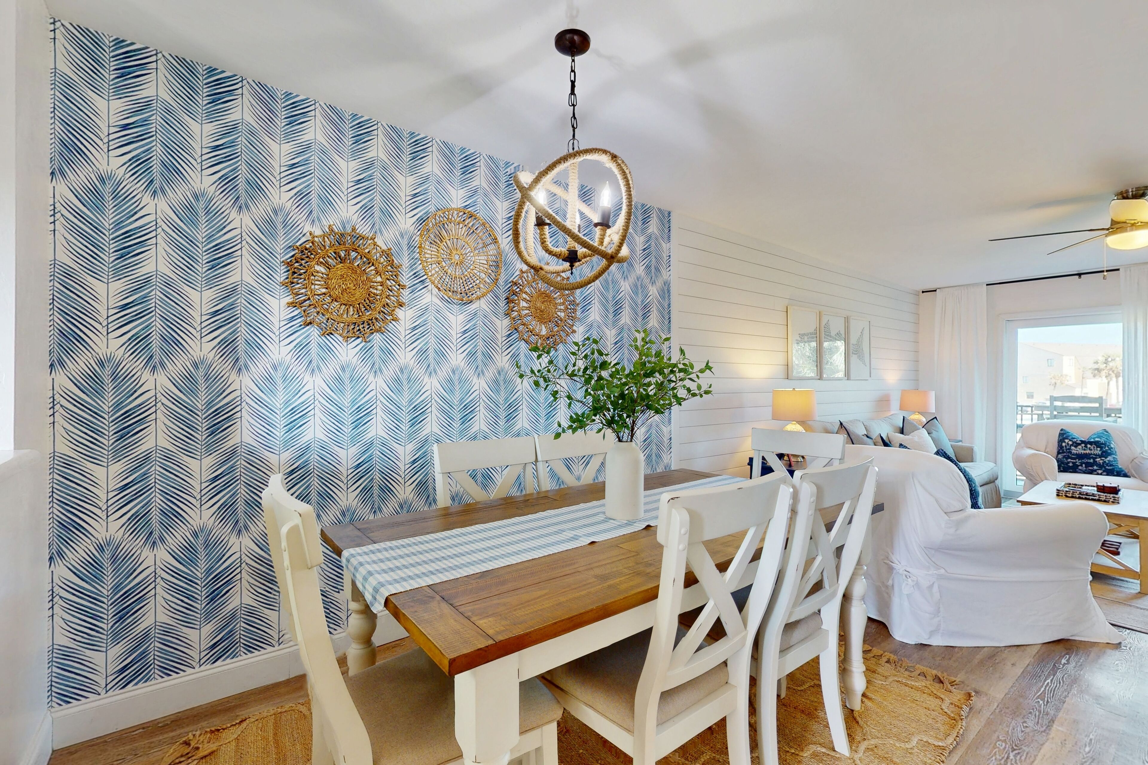 Een eetgedeelte met een houten tafel en witte stoelen, een behang met patroon, en een hanglamp.