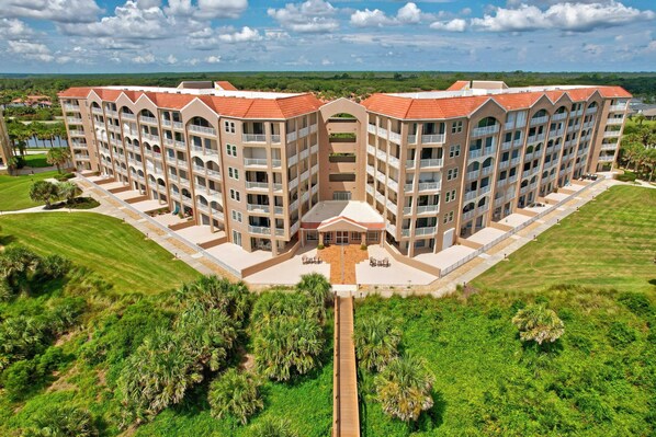 A multi-story hotel with a symmetrical facade, central courtyard, and surrounding greenery. - Oceanfront Condo With Large Patio, Direct Water Access, Pool, Central AC, & W/D (Palm Coast)