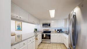 A modern kitchen with white cabinets, a stainless steel refrigerator, a microwave, and an oven. - Oceanfront Condo With Private Balcony, Shared Pool and Beach Access (Fernandina Beach)