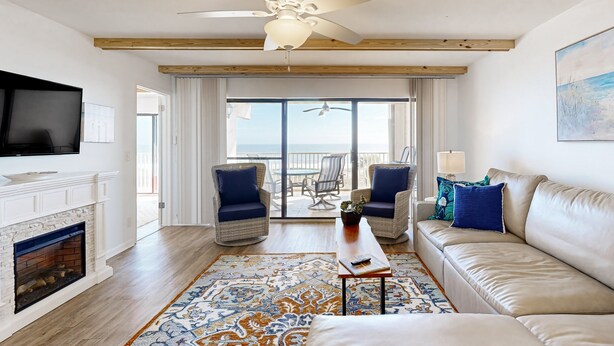 A living room with a fireplace, a ceiling fan, a sofa, and a view to the outside. - Oceanfront Condo With Private Balcony, Shared Pool and Beach Access (Fernandina Beach)