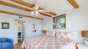 A bedroom with a bed, a blue chair, a white nightstand, and a ceiling fan. - Oceanfront Condo With Private Balcony, Shared Pool and Beach Access (Fernandina Beach)
