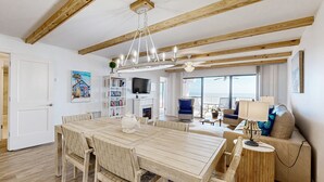 A spacious living room with a wooden dining table, a sofa, and a TV. - Oceanfront Condo With Private Balcony, Shared Pool and Beach Access (Fernandina Beach)
