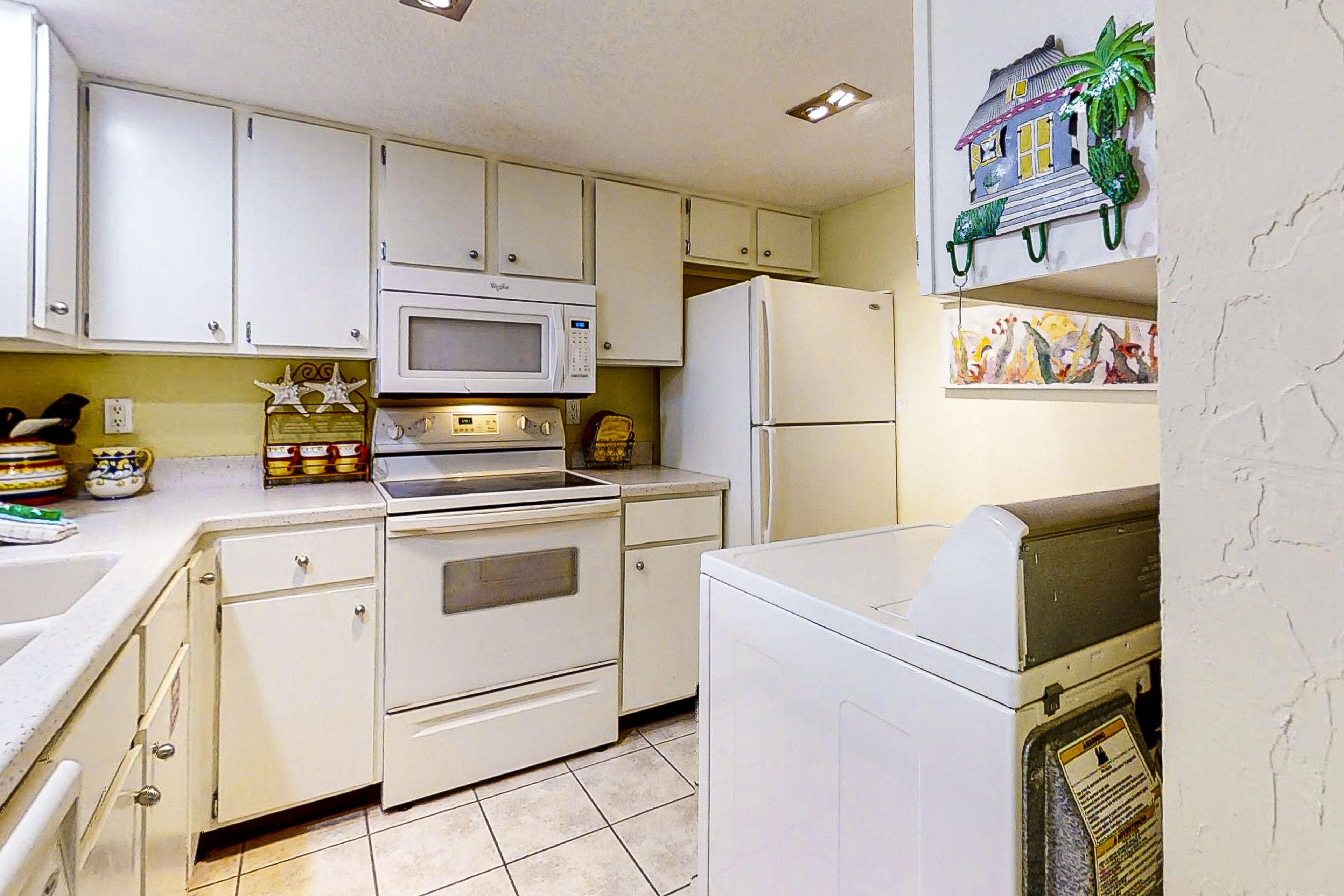 Una cocina con armarios blancos, microondas, estufa, refrigerador y lavadora.
