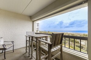A balcony with a table and chairs, overlooking a beach and ocean. - Oceanfront Condo With Pool & Tennis - Balcony, AC, Wifi & Washer/dryer (Fernandina Beach)