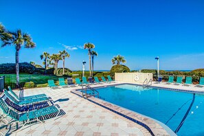 A swimming pool with blue water, surrounded by green lounge chairs and palm trees. - Oceanfront Condo With Pool & Tennis - Balcony, AC, Wifi & Washer/dryer (Fernandina Beach)