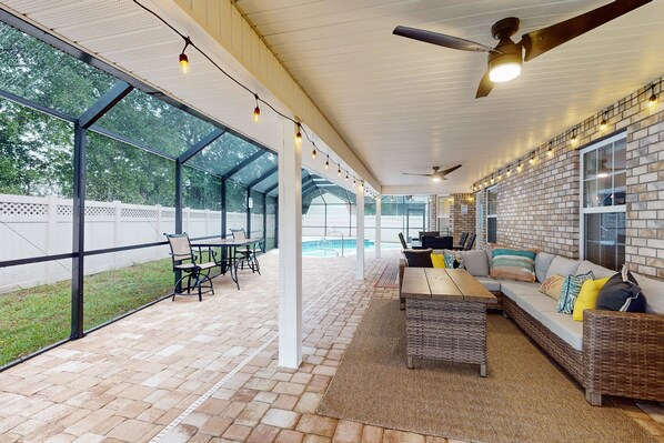 A covered patio area with a pool, outdoor seating, and a brick wall. - Spacious Home With Private Pool,spa, Gas Grill and Patio (Palm Coast)