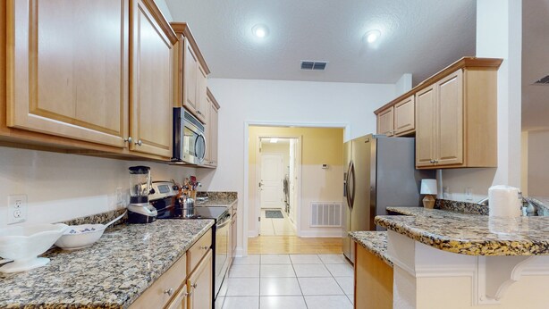 Una cocina con encimeras de granito, armarios de madera y un refrigerador de acero inoxidable.