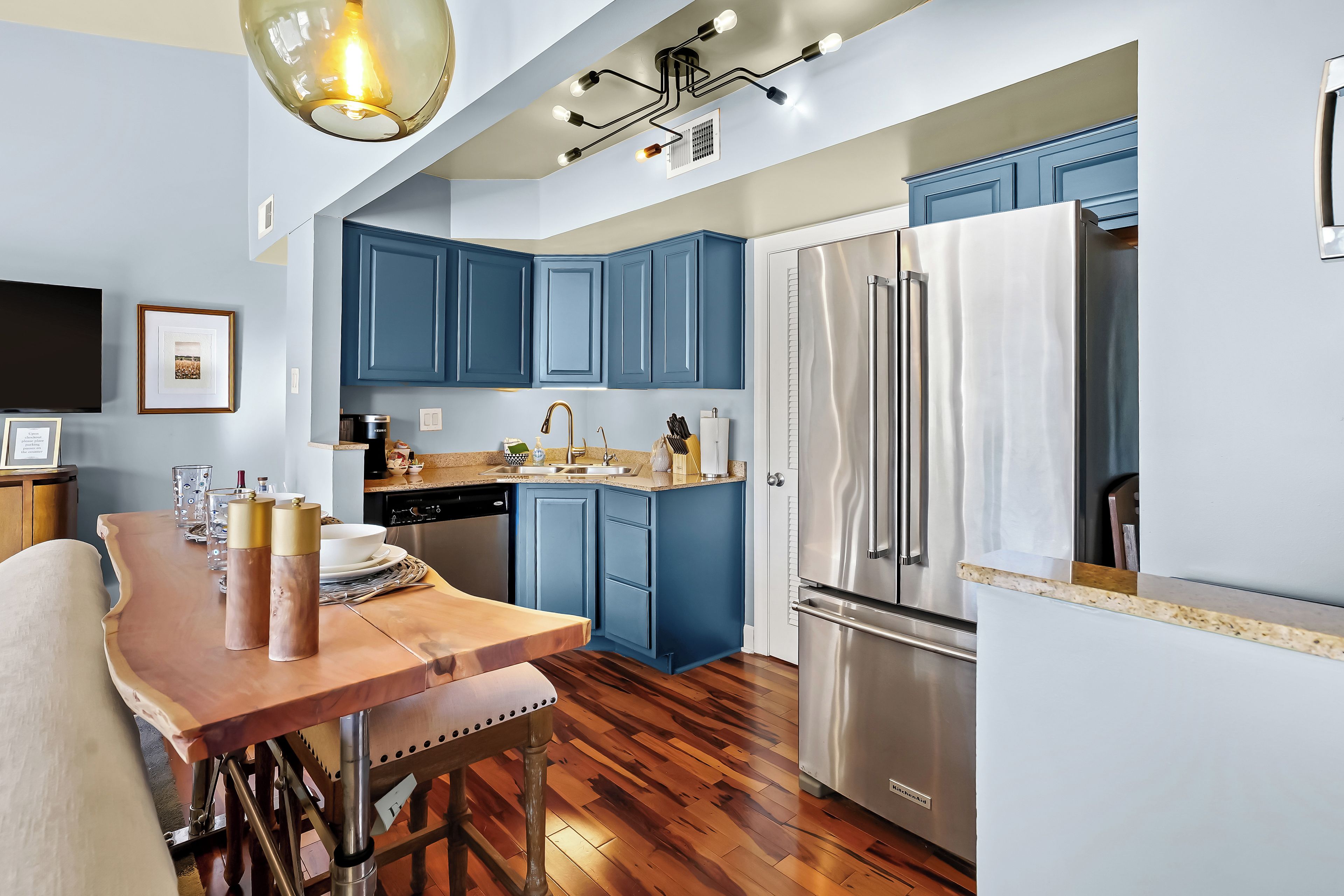 Une cuisine moderne avec des meubles de couleur bleue, un réfrigérateur en acier inoxydable et une table à manger en bois.