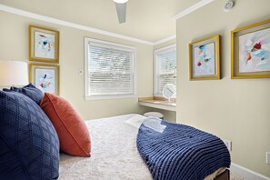 A bedroom with a bed, pillows, a bedside table, a lamp, and artwork on the walls.