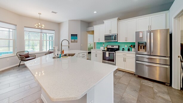 A modern kitchen with white cabinetry, stainless steel appliances, and a large island. - Updated Home With Private Pool, Patio, Central AC, & W/D (Palm Coast)