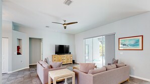 A modern living room with a sofa set, a coffee table, a TV, and a ceiling fan. - Updated Home With Private Pool, Patio, Central AC, & W/D (Palm Coast)