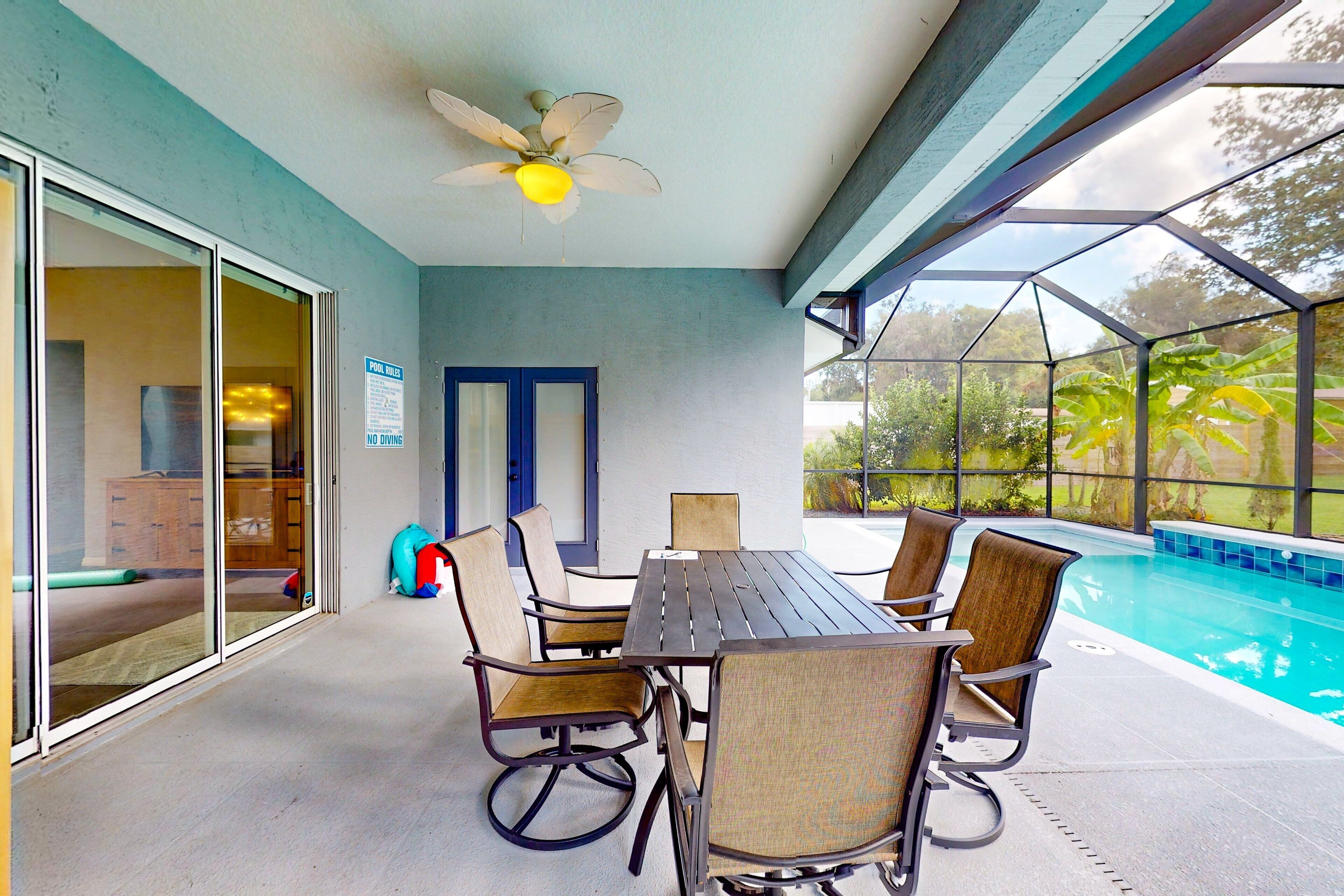 A covered outdoor area with a pool, a table with chairs, and a ceiling fan.