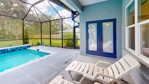 A covered outdoor swimming pool with a glass enclosure, a blue door, and white lounge chairs. - Updated Home With Private Pool, Patio, Central AC, & W/D (Palm Coast)