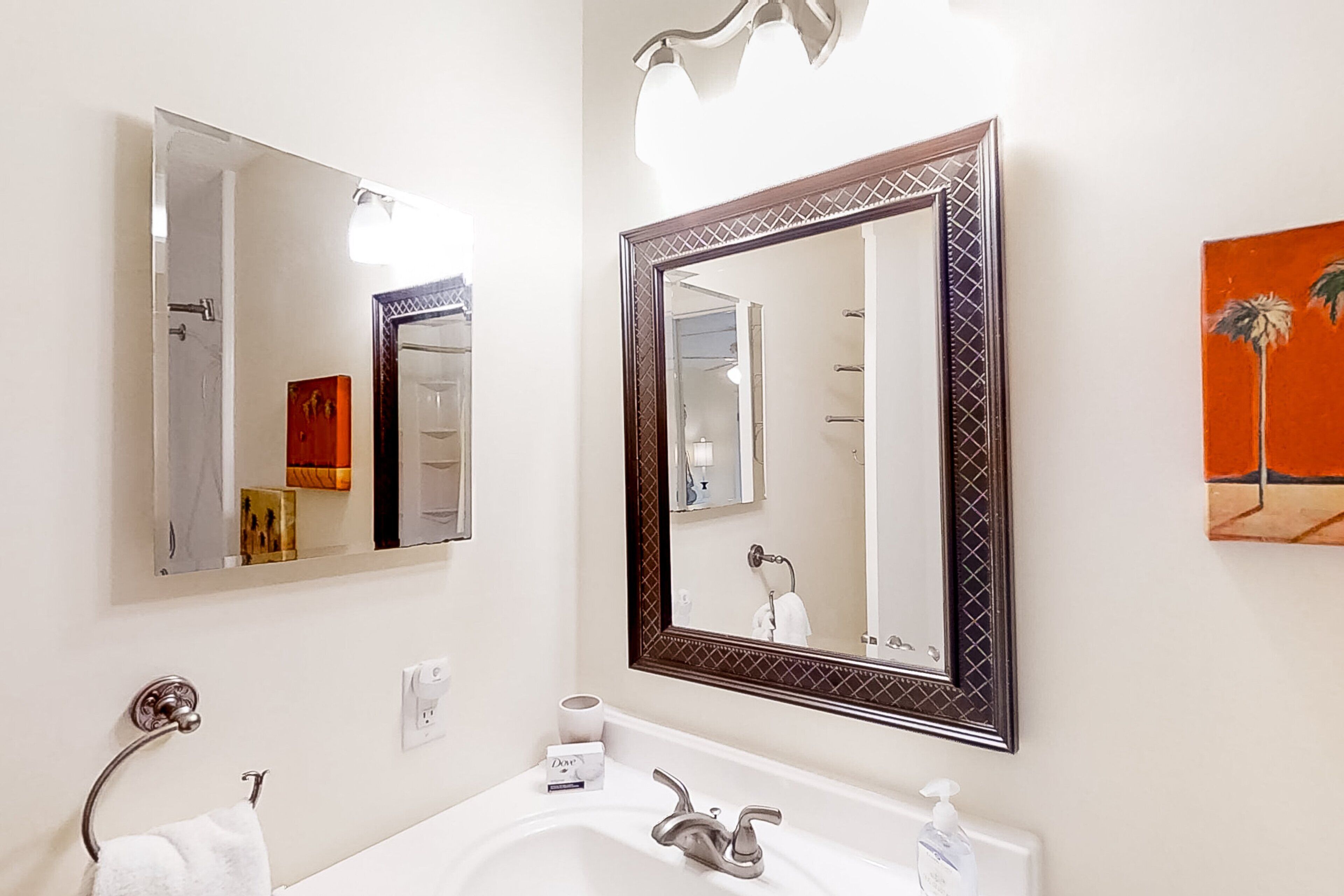 Un baño con un lavabo blanco, un espejo con marco decorativo, un perchero para toallas y un cuadro en la pared.