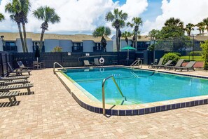 A rectangular swimming pool with a tiled edge, surrounded by a brick patio. There are lounge chairs and a lifeguard stand near the pool. - Two-story Condo With Pool, Tennis & Patio - 2 Short Blocks to the Beach (Fernandina Beach)