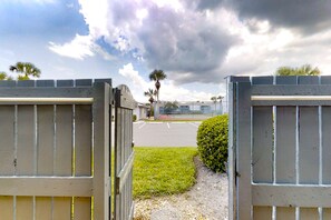 A gated entrance with a paved road leading to a building, palm trees, and a cloudy sky. - Two-story Condo With Pool, Tennis & Patio - 2 Short Blocks to the Beach (Fernandina Beach)