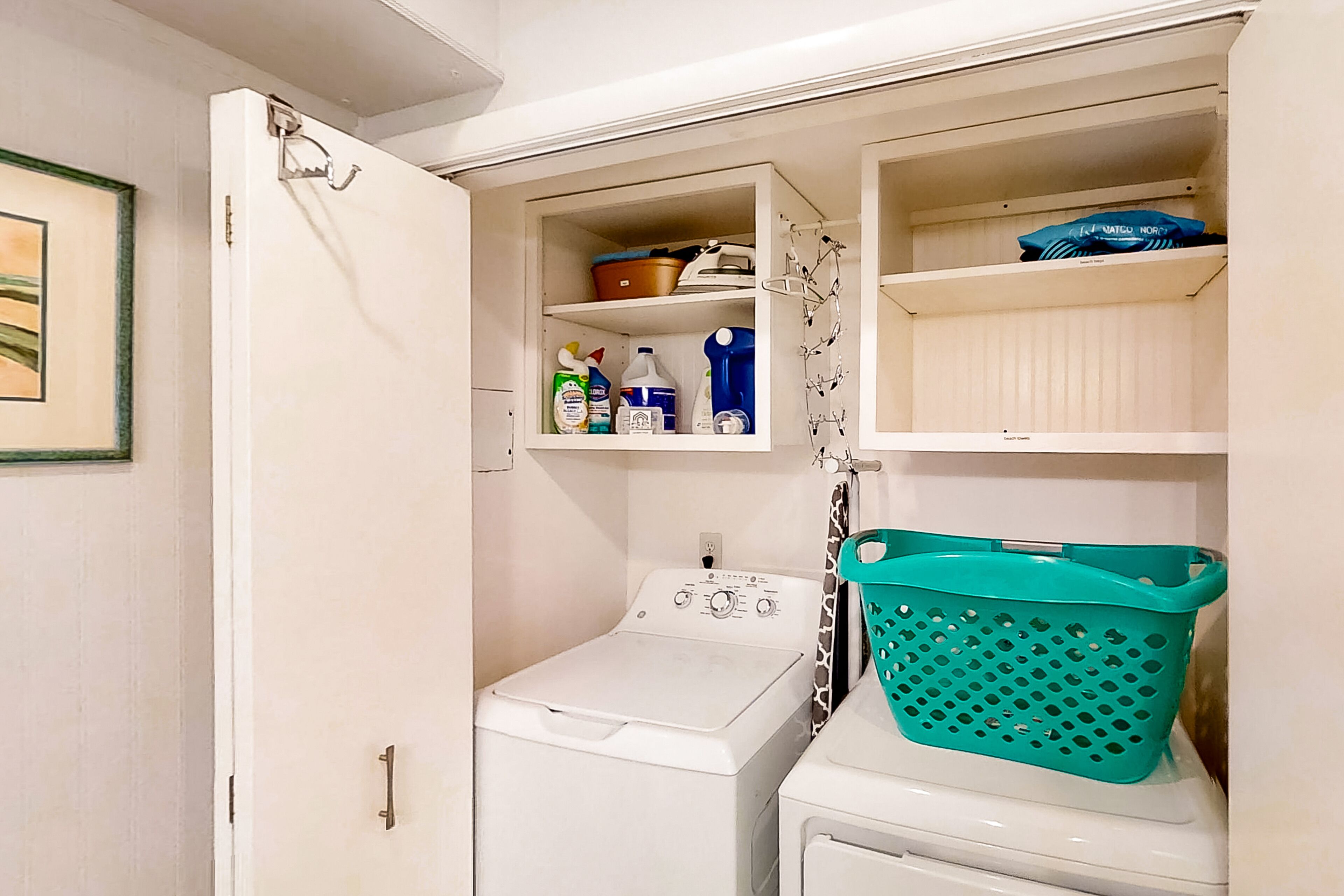 Un espace buanderie comprenant un lave-linge, un sèche-linge et une étagère où sont rangés les produits de nettoyage.