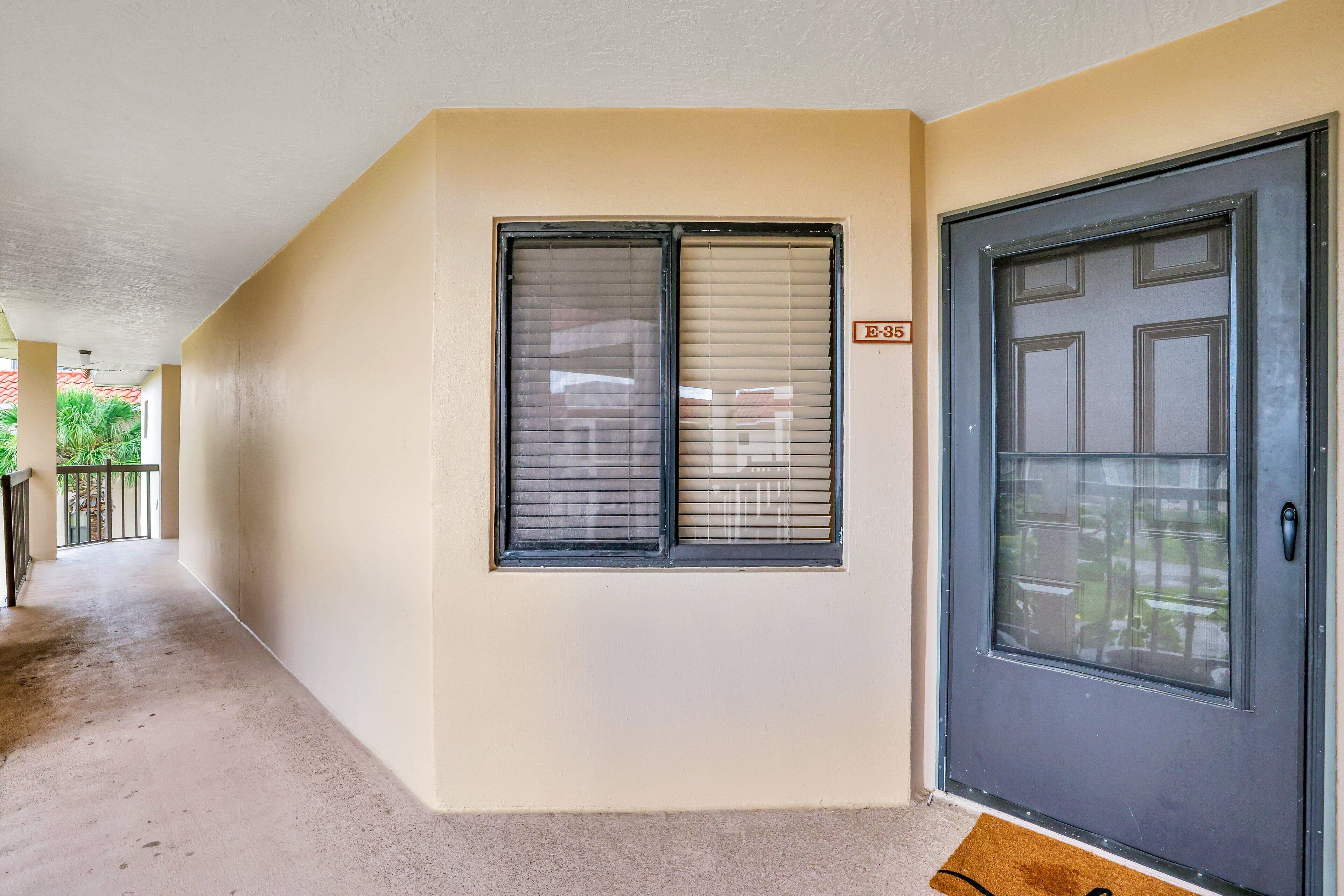 Un pasillo con pared color beige, una puerta con ventana y un cartel con el número E-35.