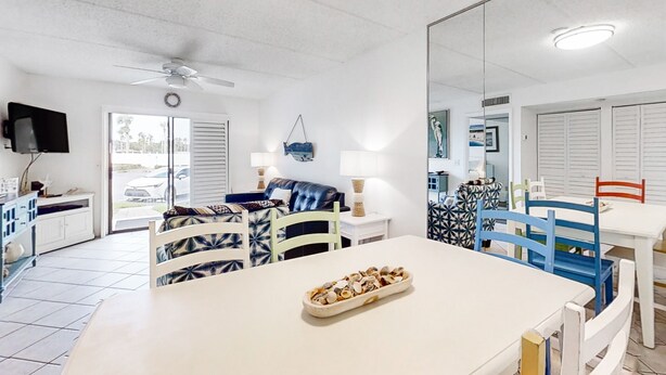 A modern, well-lit room with a dining table, chairs, a TV, and a large mirror. - Sunny Ground-floor Condo W/private Patio, W/d, On-site Pools, Tennis Court, BBQ (St. Augustine)