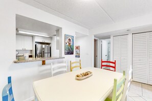 Una cocina moderna con armarios blancos, un refrigerador de acero inoxidable y un comedor con mesa y sillas.