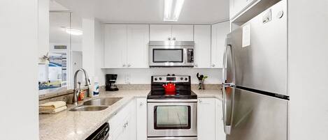A modern kitchen with white cabinets, stainless steel appliances, a dishwasher, and a granite countertop.