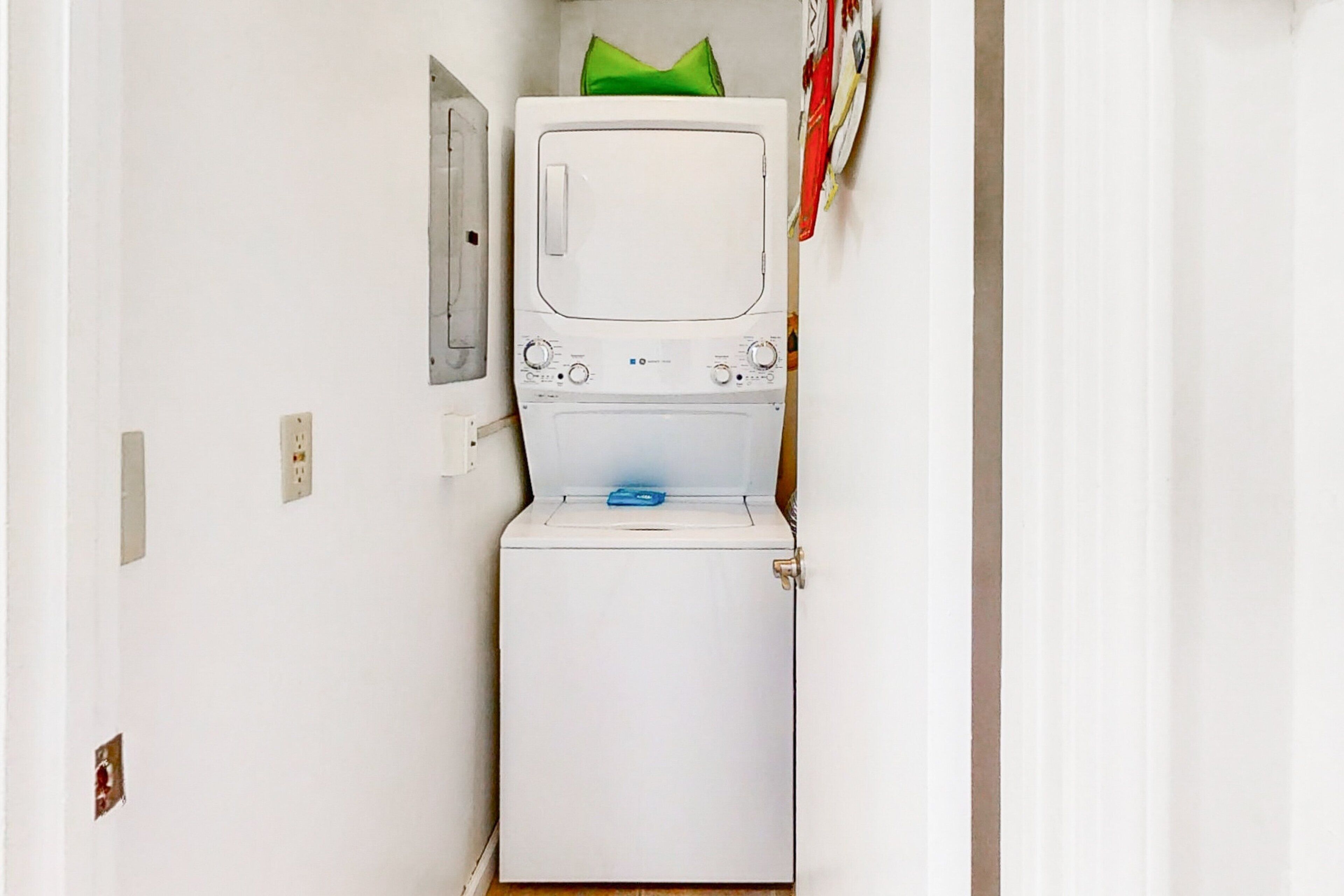 Een kleine, witte wasruimte met een wasmachine en droger, een groene handdoek op de droger, en een deur met een klein raam.