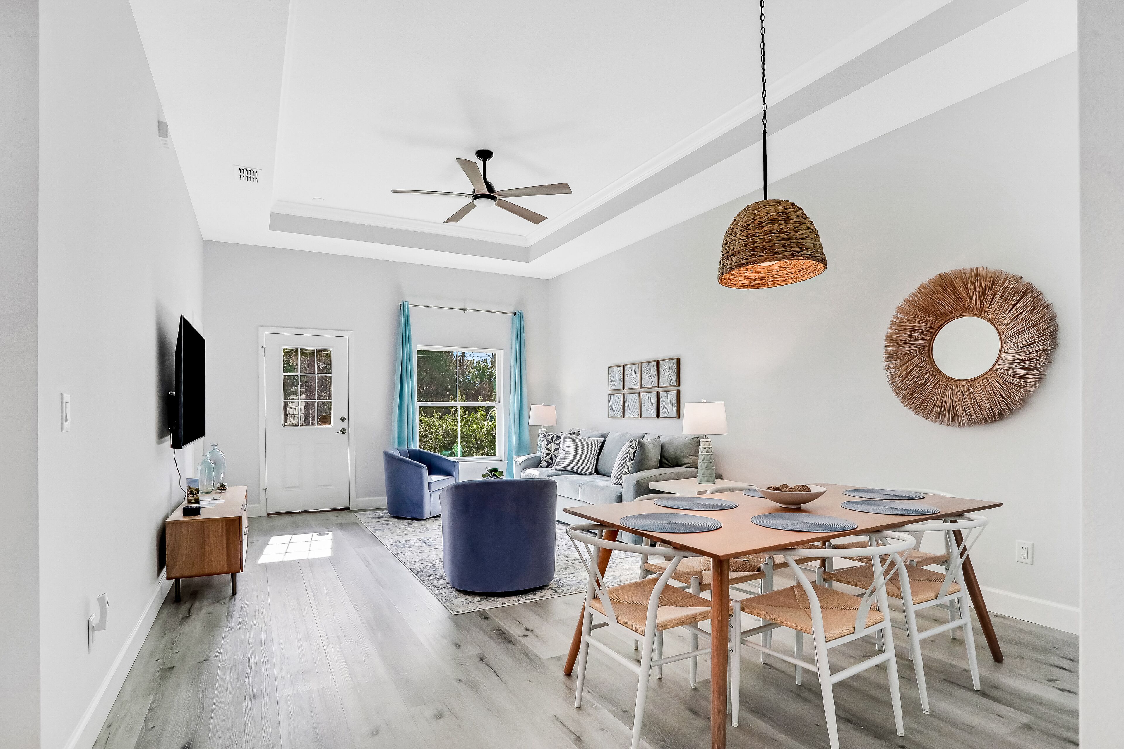 A modern living room with a dining area, a ceiling fan, and a large window with blue curtains.