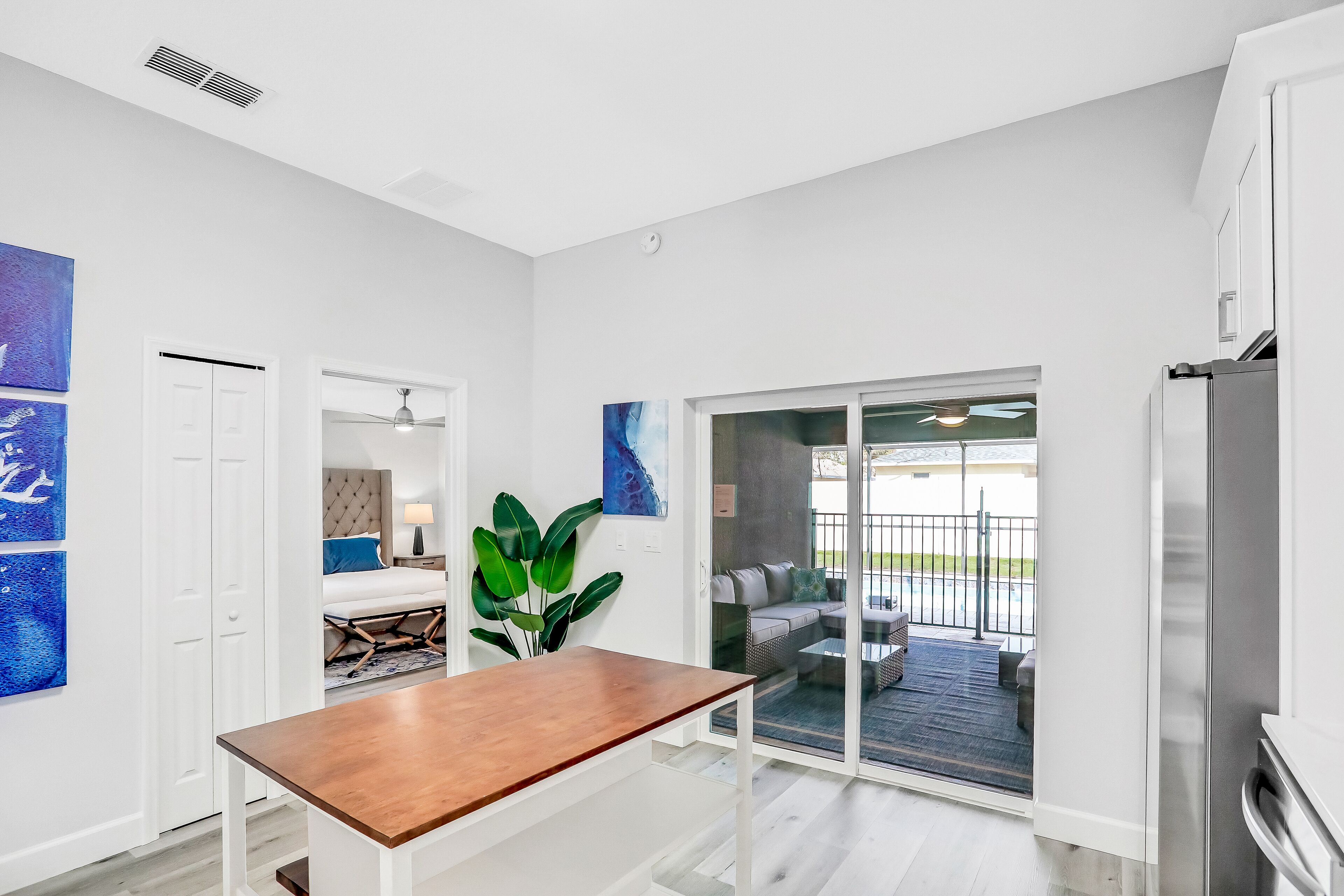 A modern kitchen with a wooden table, white cabinetry, and a sliding glass door leading to an outdoor seating area.