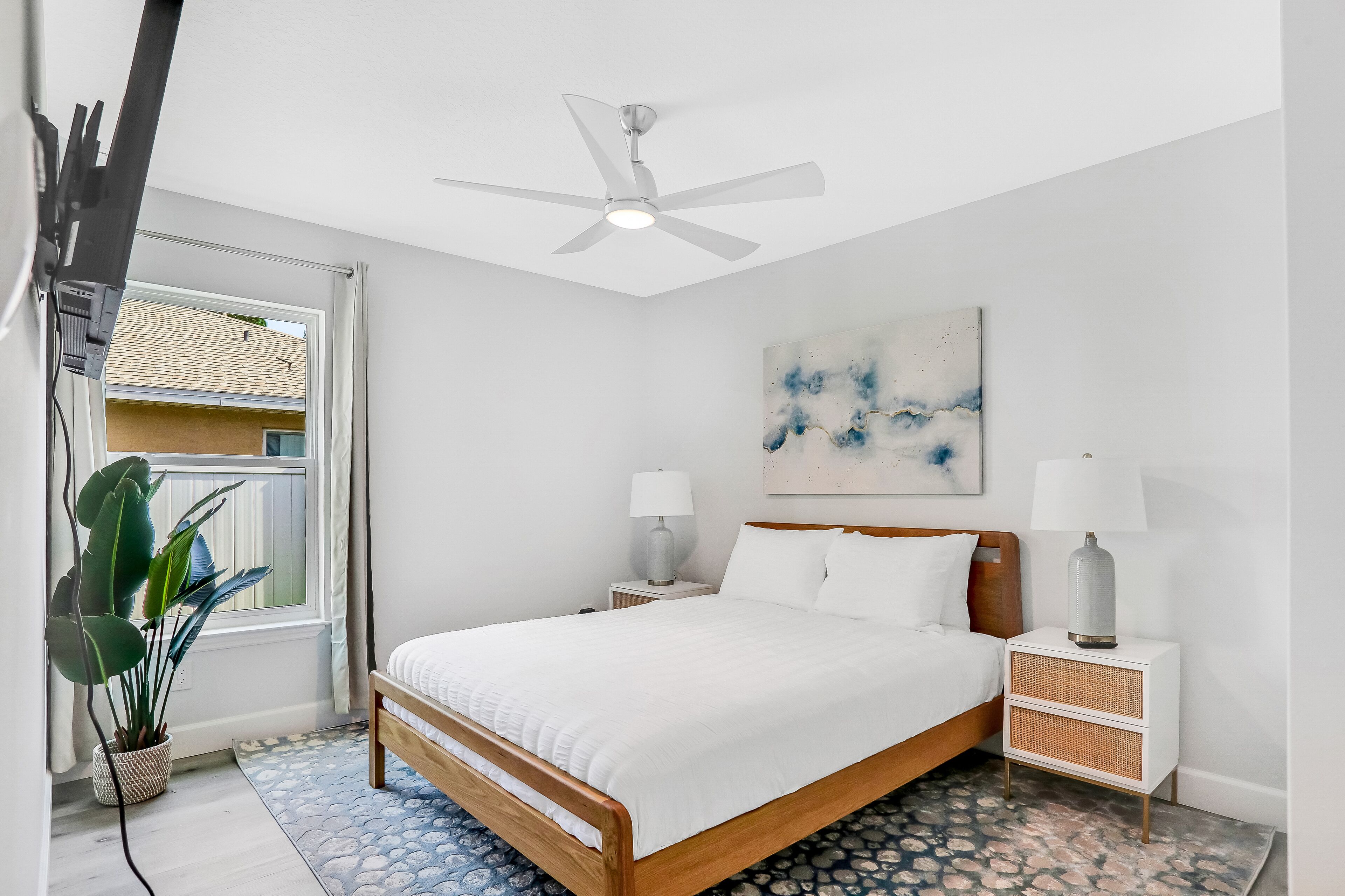 A bedroom with a bed, bedside tables, a ceiling fan, a window, and a plant.