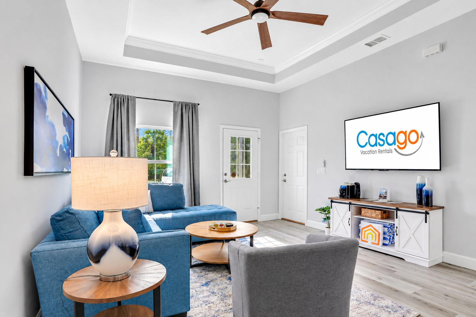 A modern living room with a sofa, armchair, and coffee table, a ceiling fan, and a TV displaying 'Casago Vacation Rentals'.