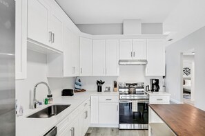 A modern kitchen with white cabinetry, stainless steel appliances, and a wooden countertop. - Twin Villas With Private Pools, Furnished Lanais, & All-new Interiors (Palm Coast)