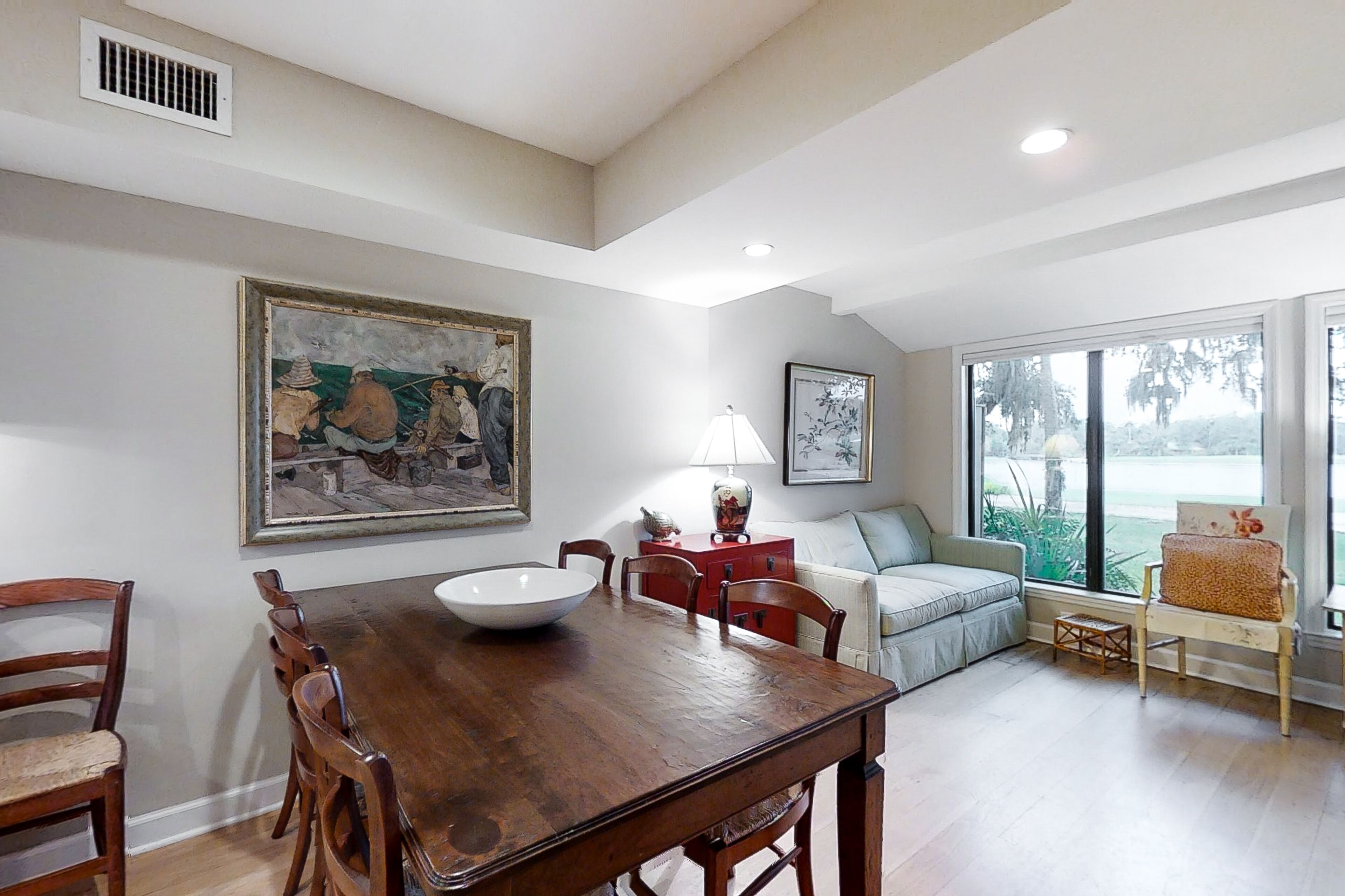 A dining area with a wooden table and chairs, a white bowl, and a painting on the wall.
