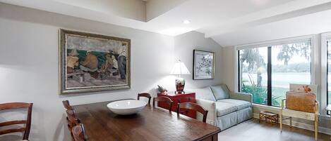 A dining area with a wooden table and chairs, a white bowl, and a painting on the wall.