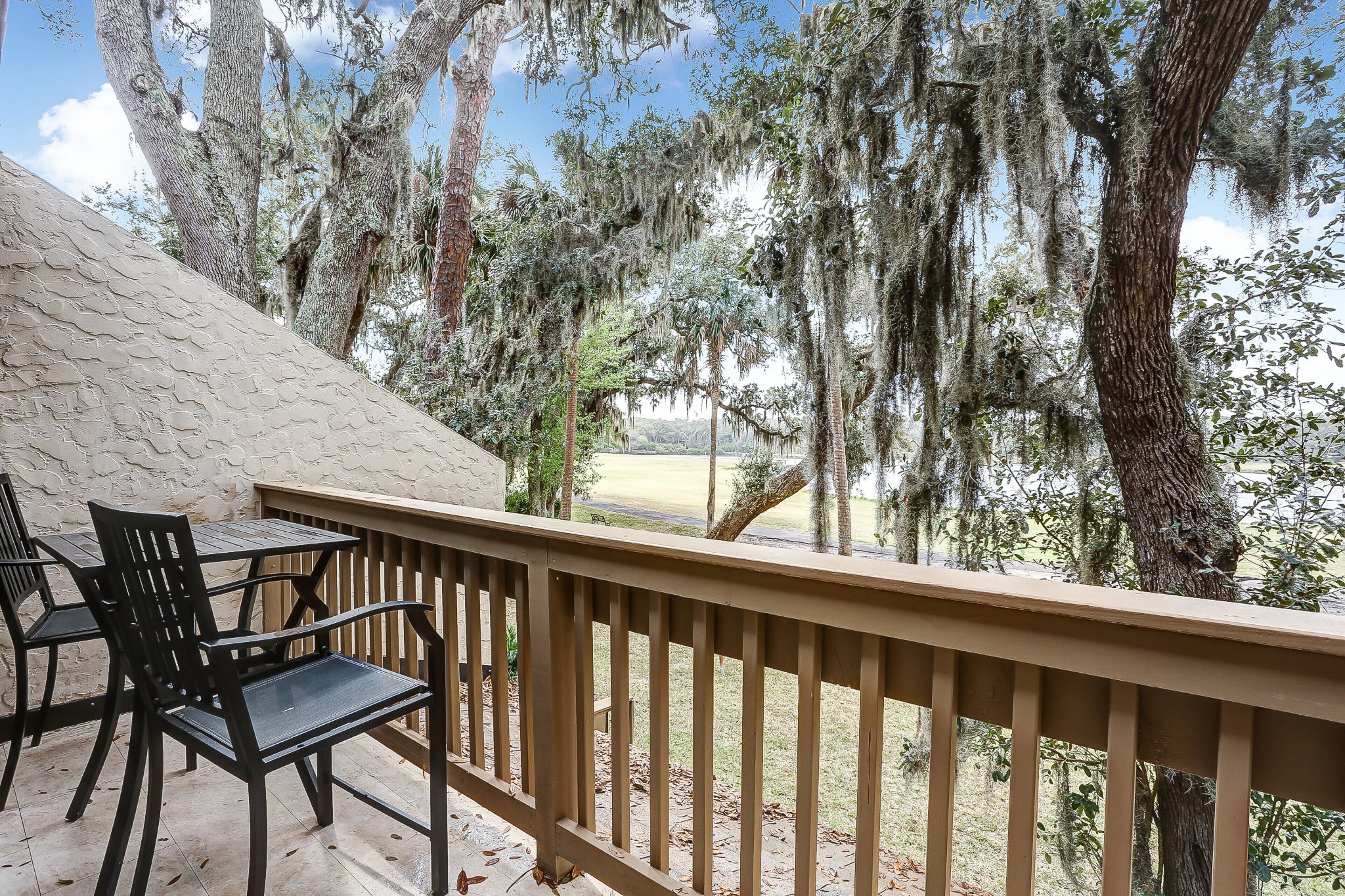 A balcony with a wooden railing, black chairs, and a view of trees and a golf course.