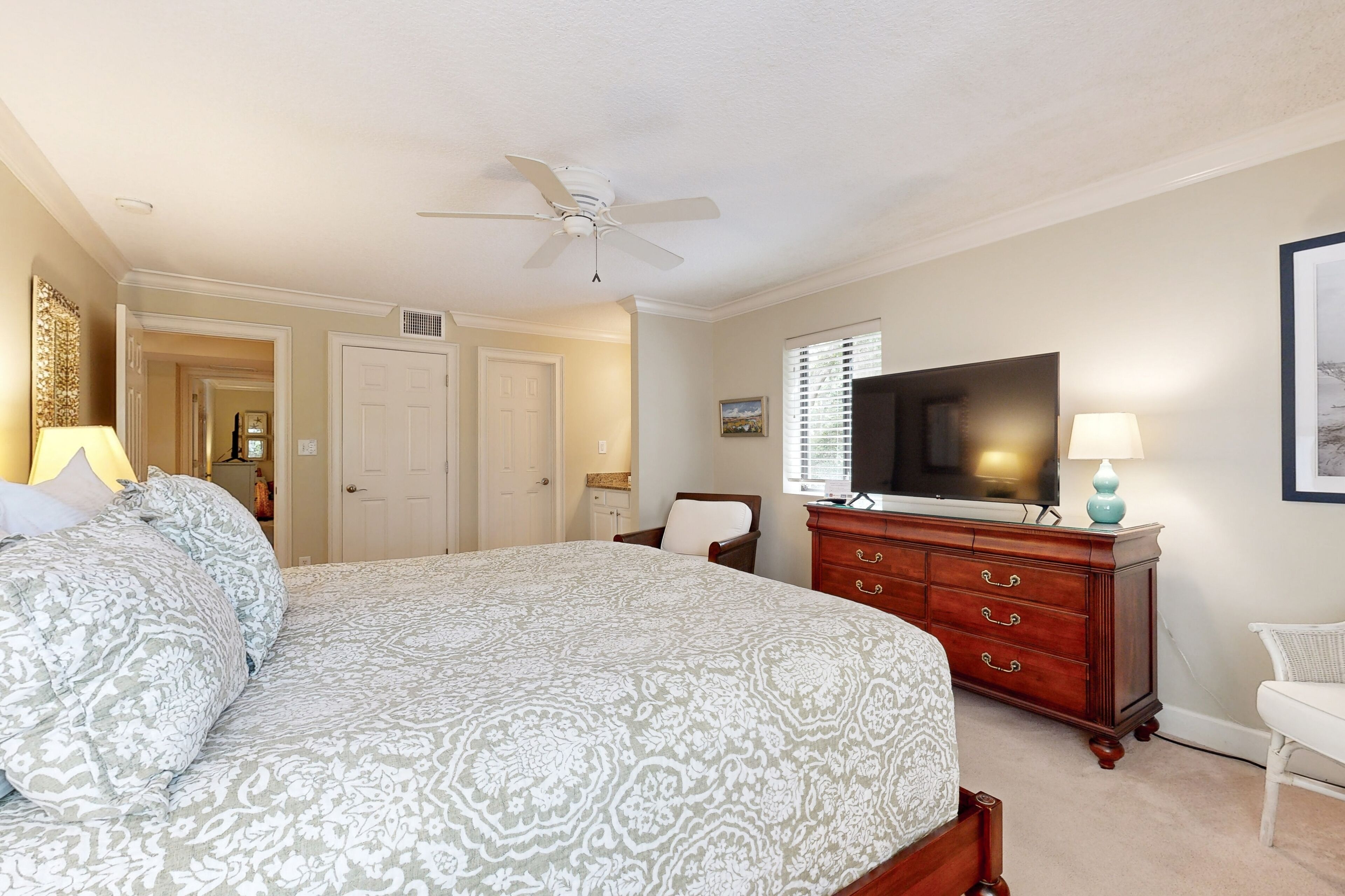 A bedroom with a bed, a dresser, a television, and a ceiling fan.