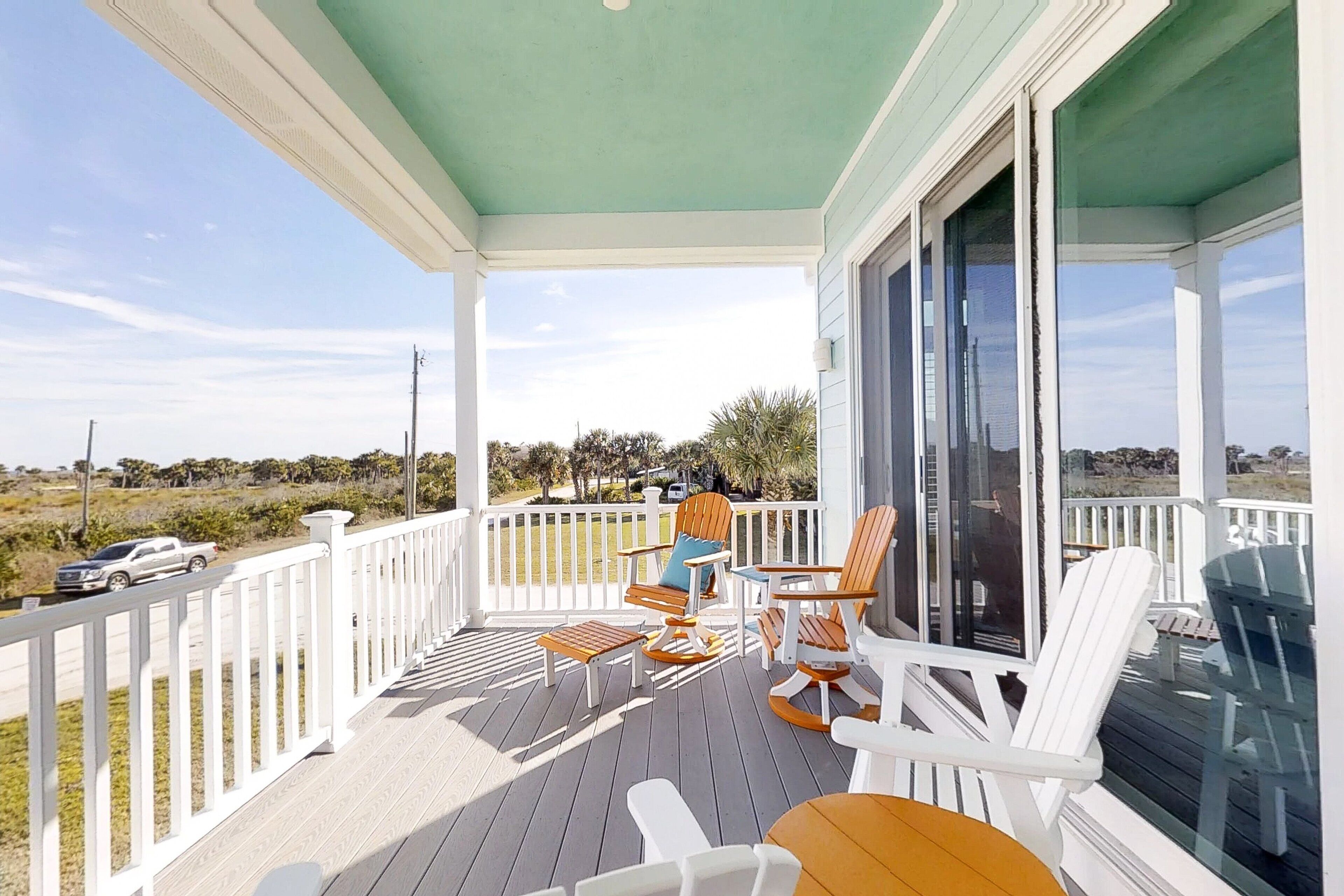 A covered porch with white railings, outdoor furniture, and a view of the landscape.