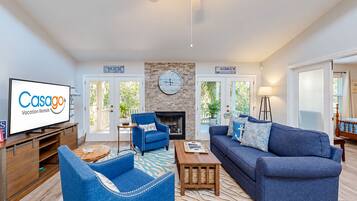A living room with a television displaying 'Casago Vacation Rentals,' a fireplace, a clock, and a view of the outdoors.