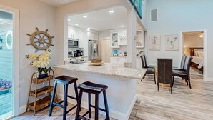 Una cocina moderna con armarios blancos, una isla central con taburetes y una rueda de barco decorativa.
