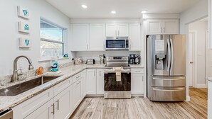 Cocina moderna con armarios blancos, electrodomésticos de acero inoxidable, encimera de granito y ventana que proporciona luz natural.
