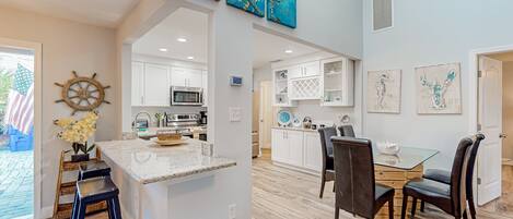 A spacious kitchen with white cabinets, a central island with stools, and a dining area with a glass table and chairs.