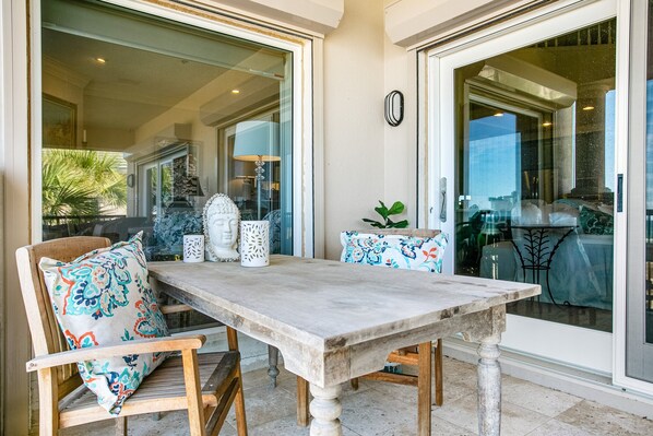 An outdoor patio with a stone table and wooden chairs, featuring patterned cushions and decorative vases. - Tranquil Coastal Home With Ocean Views, Beach Access, Balcony & Shared Pool (Fernandina Beach)
