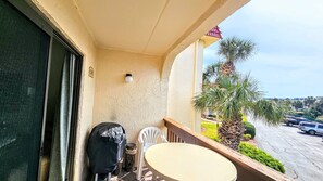 A balcony with a table and chairs, a covered grill, and a view of a parking lot and palm trees. - St Augustine Beach Retreat~ Oceanfront Resort 2 Pools Hot Tubs Pickleball, Trolley! (St. Augustine)