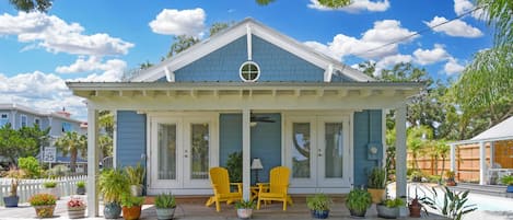 A two-story house with a covered porch, two yellow Adirondack chairs, and a small pool area.